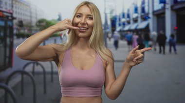Sarışın kadın, şehir sokaklarında hareketli telefon jesti için işaret parmağıyla işaret ediyor; bağlantı.