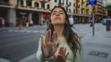 Arka planda binalarla sokakta duran bir kadın, şehir ve açık hava yaşamını vurguluyor.