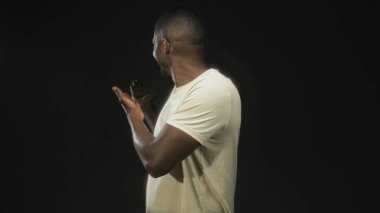 Açık eller ve görünür ön kollar ile hareket adam, bir stüdyo içinde beyaz bir tişört içinde gülümseme, profil döndü; sıcak sıcak dostça sohbet.