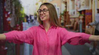 Yoğun bir şehir caddesinde canlı pembe gömleğiyle şükranlarını ifade eden kadın, arka planda bulanık yayalarla dolu canlı bir açık hava ortamında neşeli bir etkileşim ve şehir canlılığını somutlaştırıyor..