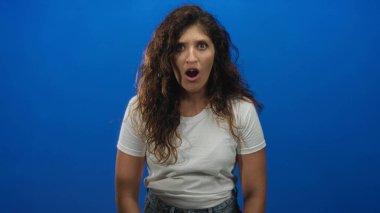 Ağzı açık, elleri havada, beyaz tişört ve kot pantolon giyen bir kadın..