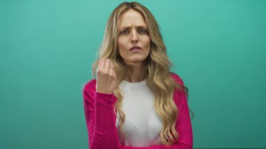 Beyaz tişörtlü, uzun sarı saçlı ve pembe kazaklı bir kadın yeşil duvar arkasında kafa karışıklığı yaratıyor..
