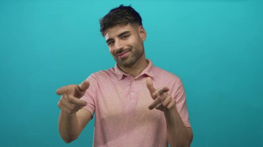 İspanyol adam iki işaret parmağını da stüdyoda yüzsüz bir sırıtışla deniz mavisi duvarına karşı gösteriyor..