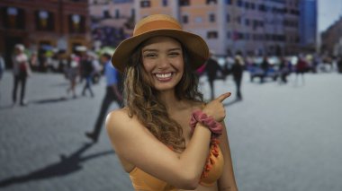 Turuncu bikinili genç İspanyol kadın gülümsüyor ve kalabalık caddede parmaklarını sağa sola gösteriyor; yaz eğlence mutluluğu heyecanı.