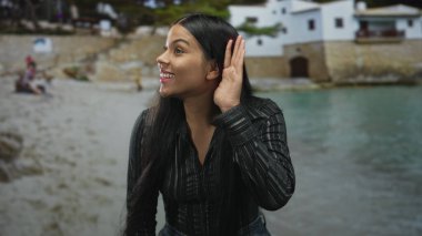 Plaj evleri yakınlarındaki sakin deniz kenarındaki kumlu sahil şeridini dinleyen genç Latin bir kadın..