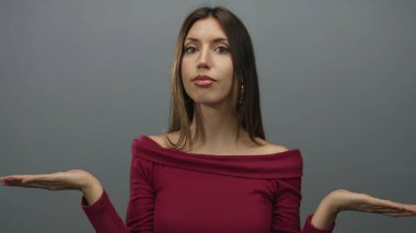 Genç İspanyol kadın gri stüdyoda poz veriyor. Elleri havada, bordo bir bluz giyiyor. Belirsizlik..