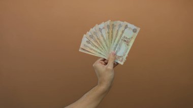 Kahverengi bir duvara karşı para dolu bir el ele tutuşmuş. Kafkasyalı bir erkek, izole edilmiş bir para sergiliyor..