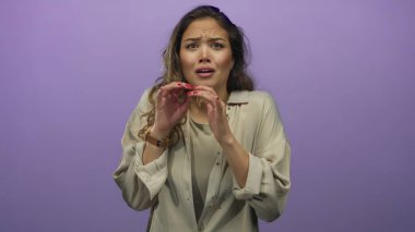 Genç bir kadın, mor bir stüdyo ortamında yüzünün yanında korkmuş ifade ve eller gösteriyor; korku..