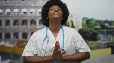 Beyaz üniforma giyen kadın doktor ve steteskop ellerini katlayarak dua ediyor..