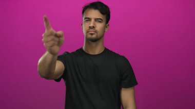 Siyah tişörtlü genç Latin bir adam canlı pembe arka planda parmak göstererek odak ve yönü aktarıyor..