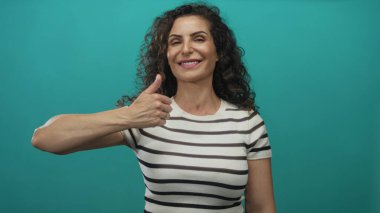 Turkuaz stüdyoda gülümseyen kadın başparmak hareketi yapıyor; pozitiflik güven iyimserlik teşvik.