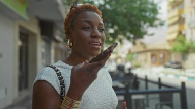 Genç Afro-Amerikalı kadın, güneşli bir caddede dükkanların arasında akıllı telefonu ağzına tutuyordu..