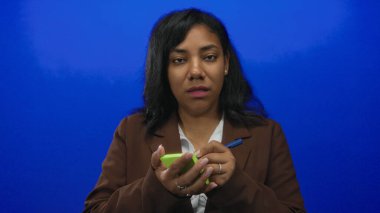 Afro-Amerikalı kadın elinde yeşil not defteri ve kalemle mavi stüdyo ortamını işaret ediyor..