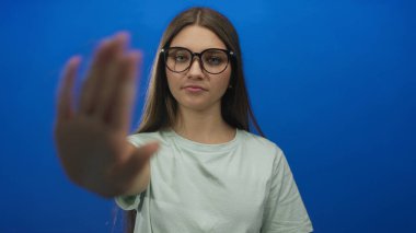 Kafkasyalı genç bir kız, avucunun içi kamerayla mavi bir stüdyo duvarına bakacak şekilde el ele tutuşuyor..