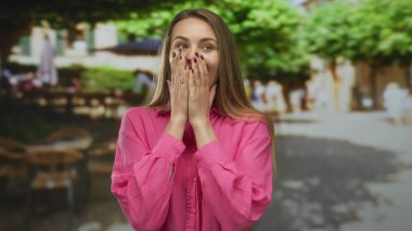 Güneşli bir şehir caddesinde, bulanık binalar ve ağaçlarla gülümseyen bir kadın, şaşkın, neşeli bir ifadeyle kentsel anı yakalıyor..