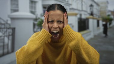 Sokakta elleri kafasında bağıran, sarı kazak giyen bir kadın şehir ortamında duygu ve hayal kırıklığını gösteriyor..