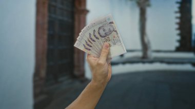 Şehir sokaklarında tek başına dolar tutan bir adam, canlı bir şehir ortamında finansal işlemleri vurguluyor..