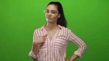 Çizgili tişörtlü genç İspanyol kadın işaret parmağıyla göğsüne yeşil stüdyoda gözlük takıyor gururlu özgüven.