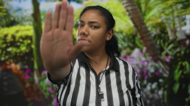 Siyah beyaz forma giyen hakem kadın, verimli yeşilliklerin ortasında, güneşli parkta avucunu ileri uzatıyor; kararlılık.