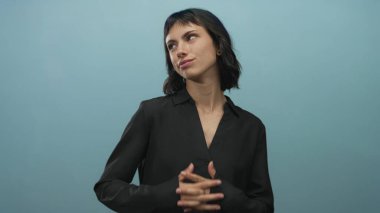 Açık mavi stüdyo göğüs kavrama genç İspanyol kadın, nazikçe gülümseme yukarı bakıyor; dinginlik.