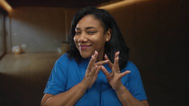 Uçsuz bucaksız stüdyoda gülümseyen mavi tişörtlü bir kadın, sakin ve düşünceli bir kadın..