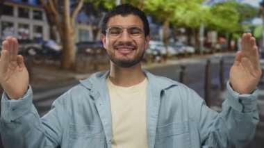 İnsan, işlek caddede, yeşil ağaçların altında ve arkada park edilmiş arabaların altında elleri ile genişliği ölçer; mutluluk değerlendirmesi.