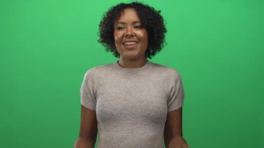 Stüdyoda elleri ağıza dolayan, parlak yeşil arka planlı, dikkat çekici bir kadın..