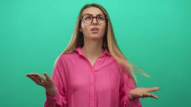 Pembe gömlekli genç bir kadın, izole edilmiş yeşil arka plan duvarına karşı anlamlı bir şekilde hareket ediyor..