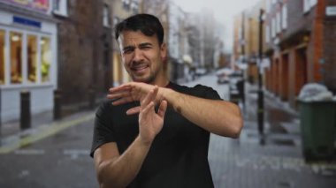 Genç İspanyol adam, şehir binalarının bulanık olduğu bir caddede elleri havada korku gösteriyor..