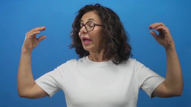 Orta yaşlı İspanyol kadın bir stüdyo ortamında elleri ve kolları ile hareket; iletişim ifadesi nişan konuşması.