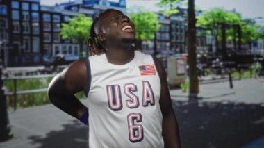 Amerika 'da Jersey' li bir adam şehrin aşağısında, yüzünü buruşturuyor ve bayraklarını gösteriyor; ağrı kesici.