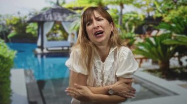 Kolları çapraz bağlanmış bir kadın otel havuzunda el ele tutuşmuş, elleri titreyerek ağzının kenarında, soğuk..