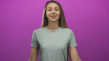 İzole edilmiş pembe arka planda gülümseyen, elleri birbirine kenetlenmiş, sıradan bir gömlek giyen, stüdyo ortamında sıcaklığını ve mutluluğunu ifade eden bir kadın..