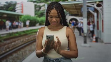 Demiryolu rayları görünür olan sokak platformunda akıllı telefonu dinleyen kadın; günlük bağlantı memnuniyeti.