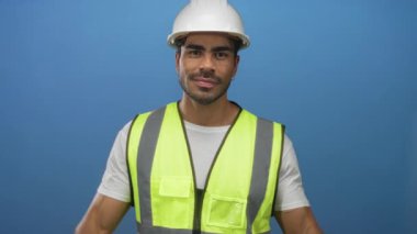 Beyaz şapkalı ve neon yelekli adam mavi stüdyoda Ziyaretçi tabelası yaparken ellerini kaldırıyor..