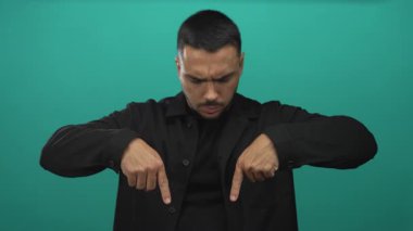 Kırış kırış kaşlı genç İspanyol adam her iki işaret parmağını da yeşil stüdyoda aşağı işaret ediyor; azim dayanıklılık dayanıklılığı.