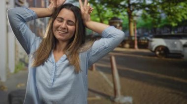 İspanyol kadının gülümsemesi, güneşli bir şehir caddesinde elleri ile tavşan kulağı yapar..