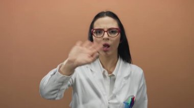 Gözlük takan bilim adamı kahverengi duvara karşı jestler yapıyor, seyircilerle irtibat kuruyor, profesyonel çevreyi ve iletişimi vurguluyor.