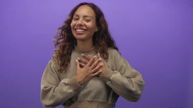 Stüdyoda elleri göğsünde gülümseyen genç Afrikalı Amerikalı kadın canlı mor arka planda; minnettarlık samimiyetle.