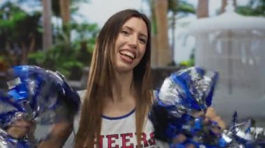 Beyaz üniformalı ponpon kız metalik mavi ponponu tutuyor ve ormanda enerjik bir şekilde sallıyor; coşku..