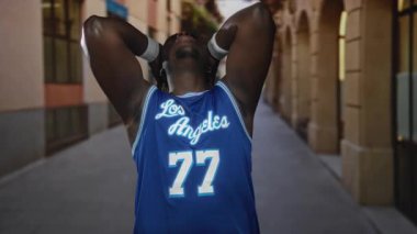 Mavi Los Angeles 'lı genç adam 77 numaralı basketbol forması. Elleri kafasında, eski kasaba sokaklarında rastaları ayarlıyor. Neşe kutlaması..