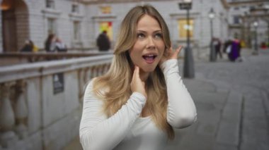 Gündüz vakti kalabalık bir şehir kaldırımında eli yanağında ve ağzı açık sarışın kadın şaşkınlık heyecanına kapıldı..
