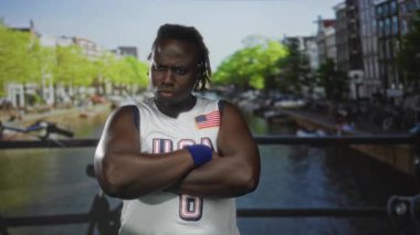 Amerika forması ve bileklik takan, caddede kolları çaprazlanmış bir adam, meydan okuma gücü gururu..