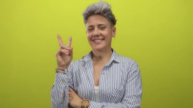 Kısa saçlı, gülümseyen beyaz kadın çizgili gömlek ve bileziklerle stüdyoda barış işareti gösteriyordu. Mutluluk..