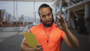 Turuncu tişört giyen adam sarı pano tutarken sağ el binada 