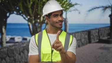 Beyaz şapka ve yansıtıcı yelek giymiş genç İspanyol mühendis parmak kaldırmayı işaret ediyor..