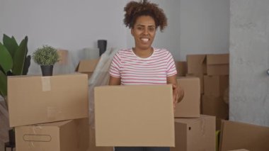 Karton kutu taşıyan ve binadaki kutuları düzenlerken gülümseyen kadın; yeni ev neşesi.