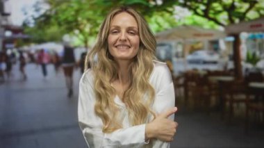 Zarif bir kadın bir restoranın içinde dudaklarını şişirirken genç sarışın bir kadın da sokağa bakan bir terasta durup gülümseyerek selamlıyor..