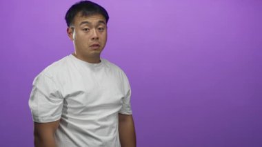 Adam stüdyoda mor arka planda beyaz tişört giyen ve tarafsız duruşu olan kameraya bakar..