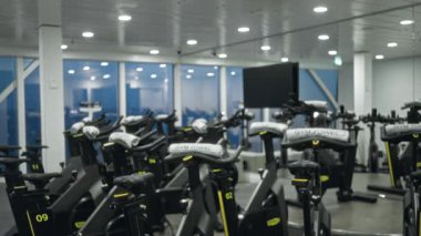 Bulanık egzersiz bisikletleri, aynalı duvarlar ve tavan lambalarıyla odaklanmış spor salonu sahnesi; arka plan arka plan arka plan kopyasıName.